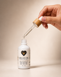 Hand holding the dropper above the Bee Bella Argan Oil bottle with a drop of oil