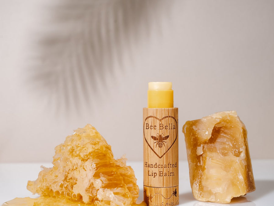 Bee Bella beeswax lip balm tube beside dripping honeycomb and a chunk of raw beeswax