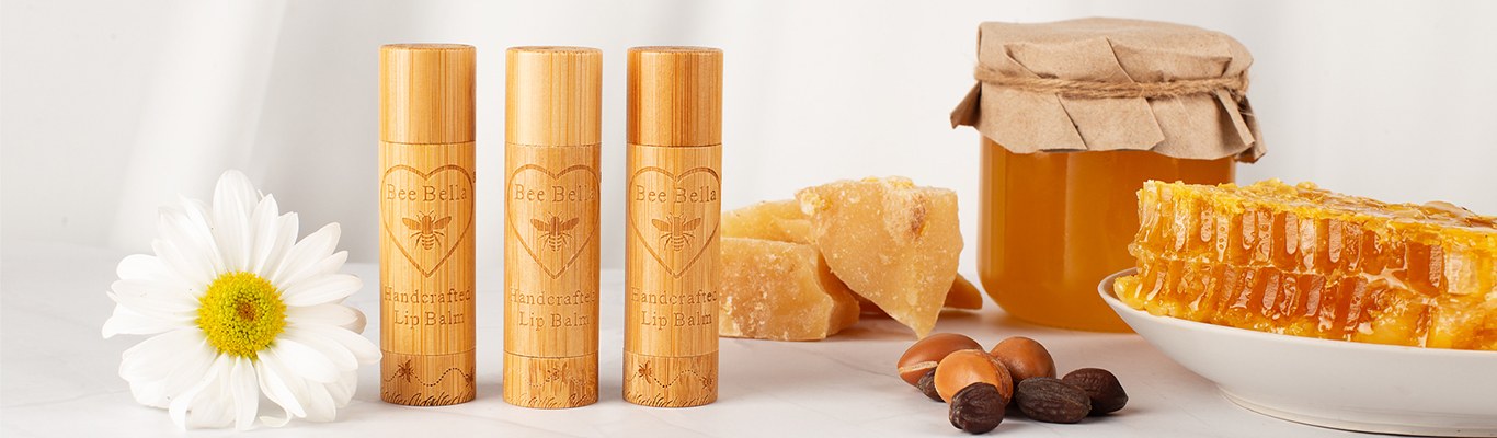 Three handcrafted Bee Bella bamboo lip balm tubes beside beeswax, honey, and honeycomb - natural Fair Trade ingredients