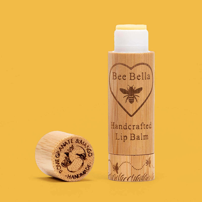 Bee Bella Pomegranate Mango lip balm in a bamboo tube shown with a orange yellow colored background